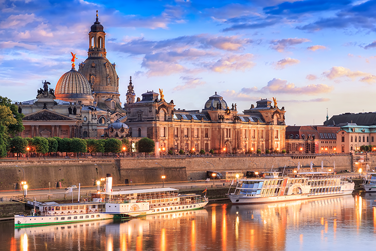 Blick auf die Brühlsche Terrasse mit historischen Gebäuden und mehreren Ausflugsschiffen am Flussufer bei Sonnenuntergang.